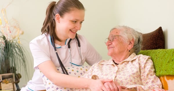 Pflegerin hält Hand der im Bett liegenden Seniorin