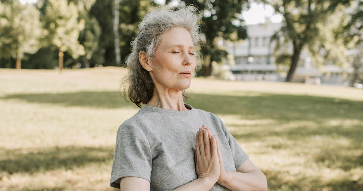Frau mit grauen Haaren atmet durch in Yoga-Position in einem Park