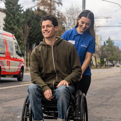 Patient im Rollstuhl und Pflegerin beim Spazieren