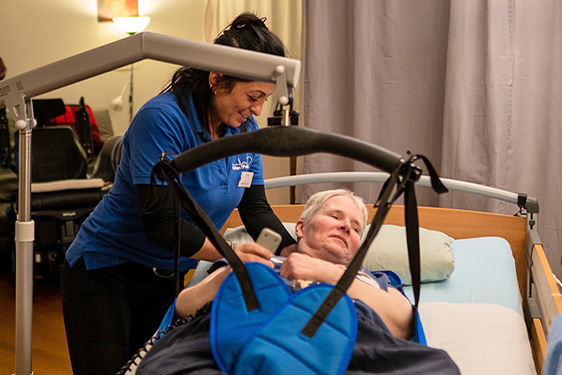 Pflegerin mit Patientin am Bett mit elektronischer Aufrichthilfe