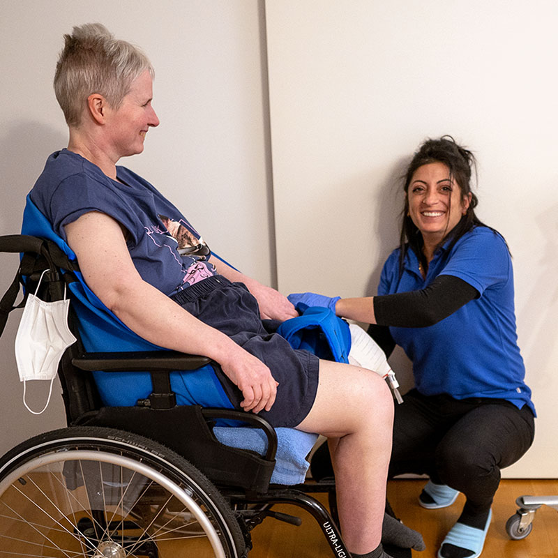 Pflegefachfrau hockt neben dem Rollstuhl einer jungen Patientin, die nach einem Unfall am Bein operiert wurde
