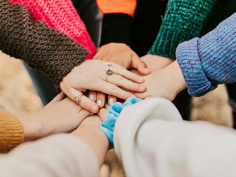 Eine Gruppe von Menschen mit übereinander gelegten Händen, die Teamgeist und Zusammenhalt symbolisieren.