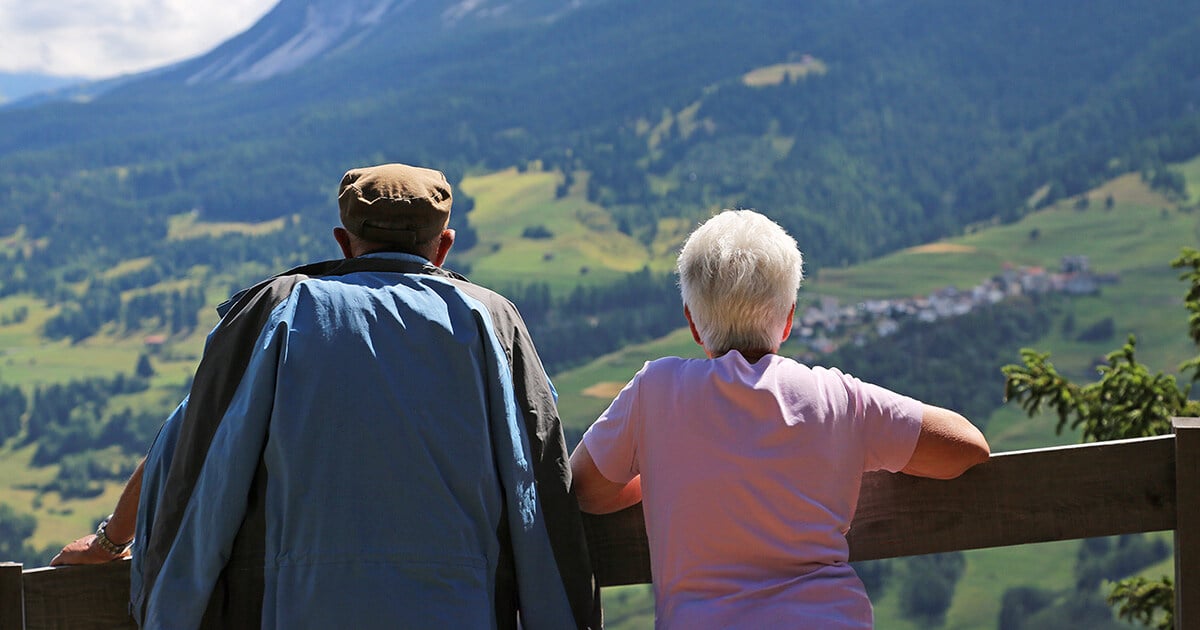 Älteres Paar betrachtet von einer Aussichtsplattform aus die malerische Landschaft der Schweizer Alpen, symbolisch für Pflegebedarf in der Schweiz