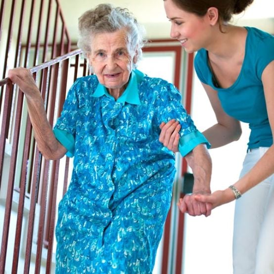 Pflegefachfrau hilft älterer Dame die Treppen hinunter