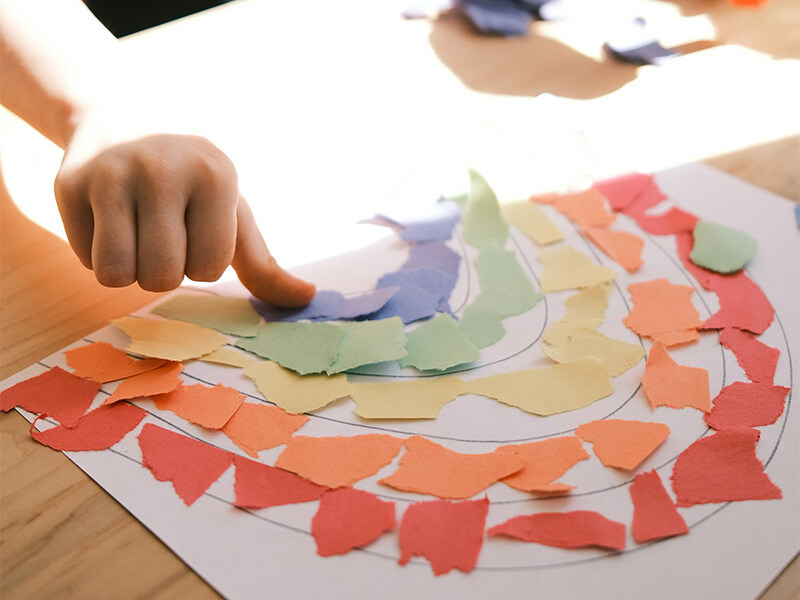 Kind beim Basteln mit bunten Papierstücken, Konzept für kreative Kinderbetreuung.