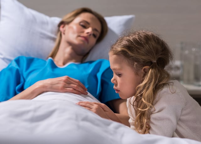 Ein kleines Mädchen sitzt am Bett der kranken Mutter