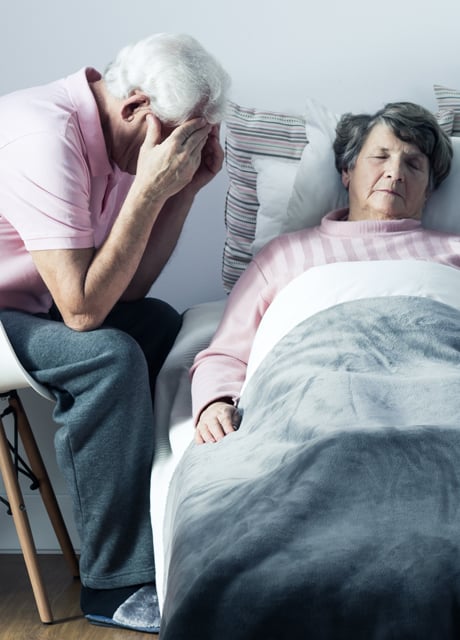 Älterer Mann sitzt am Bett seiner sterbenden Frau