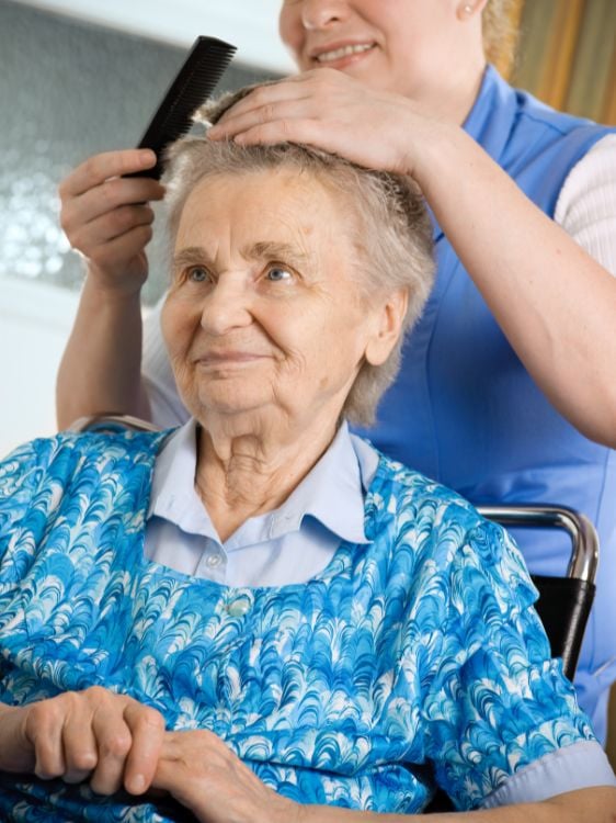 ältere Frau bekommt von Pflegerin die Haare gekämmt