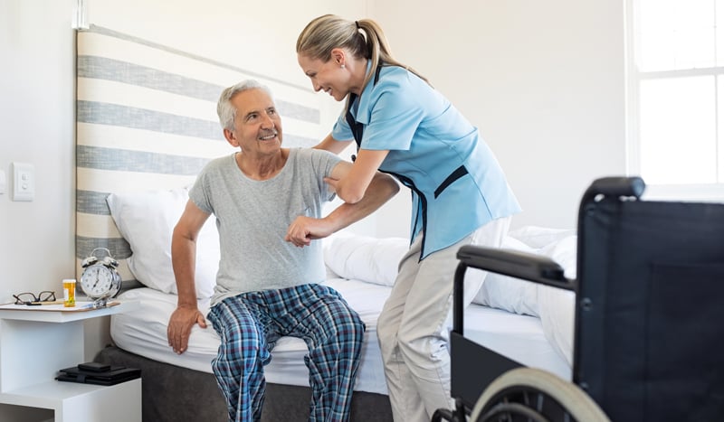 Pflegefachfrau hilft älterem Herrn aus dem Bett auszusteigen