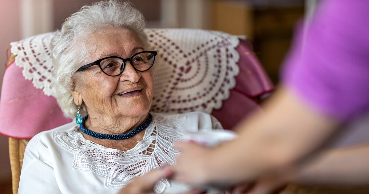 Ältere Dame genießt private Spitex-Betreuung und lächelt während ihr eine Tasse gegeben wird.