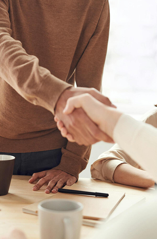 Zwei Personen geben sich in einem Büro über einem Tisch die Hand, was Fairness und professionelle Zusammenarbeit symbolisiert.