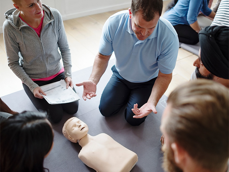 Ein Erste-Hilfe-Kurs für pflegende Angehörige, die einem Instruktor zusehen, der die Anwendung von CPR an einer Trainingspuppe demonstriert.
